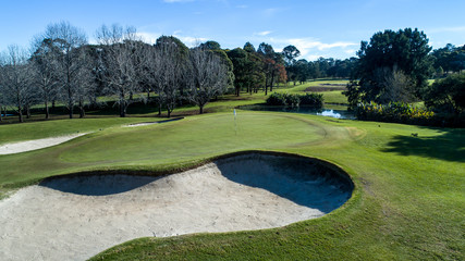 Golf course green with flag, bunkers and tree lined fairway