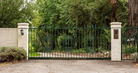 Green metal driveway entrance gates set in brick fence
