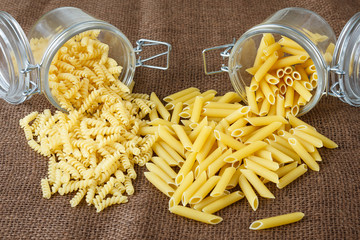 Italian pasta - penne and fusilli in glass jar on brown background