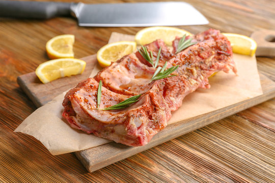 Board with raw pork ribs and lemon slices on wooden background