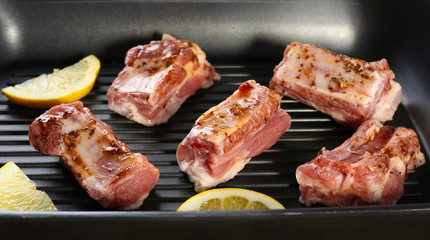 Grill pan with raw pork ribs and lemon slices on wooden table, closeup