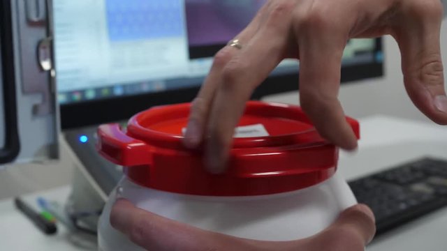 Chemical scientist opening white unlabeled plastic tank canister with chemicals on laboratory table