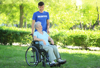 Happy senior woman on wheelchair with young male volunteer outdoors