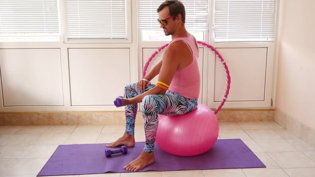 A playful handsome guy in a pink T-shirt and blue leggings is engaged in fitness depicting a girl. Slow motion