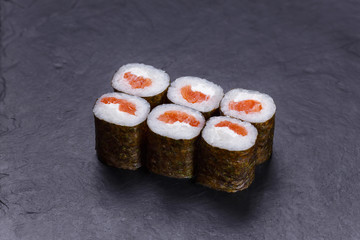 Classical Japanese cuisine, sushi rolls with salmon on black stone table. Traditional delicious food