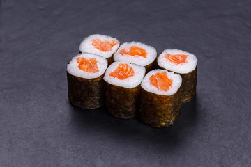 Traditional sushi rolls with raw salmon served on black slate, Japanese cuisine.