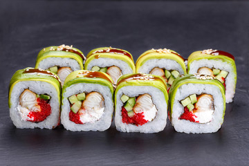 Tasty and delicious uramaki sushi rolls with smoked eel, unagi sauce and sesame covered with avocado slices