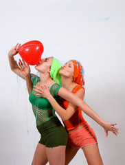 Two young girls are fighting for a red heart balloon.. One embraces the balloon while the other is...