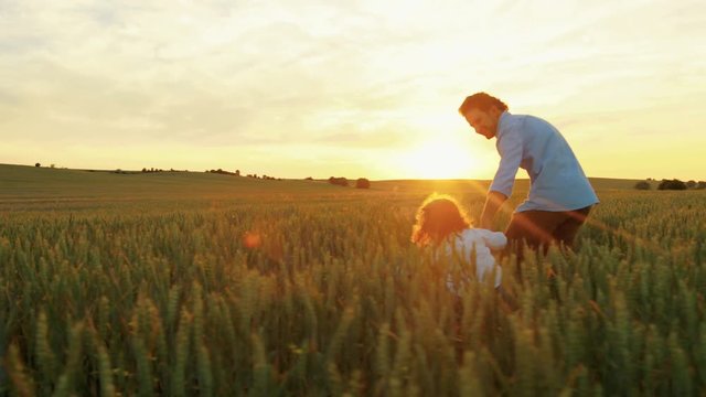 Happy father with little son runing holding hands through the green wheat field with wooden plane toy. Pretending like flying