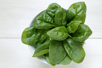 fresh baby spinach leaves on white wooden background