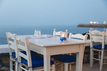 Ambient atmospheric evening on Greek coast, white tables in restaurant