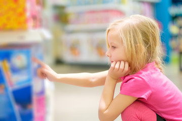 Fototapeta na wymiar Adorable girl in pink explore toys in kids supermarket