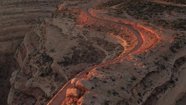 AERIAL: Black SUV car driving up the winding switchback road climbing up the mesa mountain cliff in red rock desert. 4x4 jeep vehicle traveling on steep hairpin Moki Dugway carved into the cliff edge