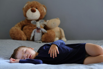 Beautiful baby boy sleeping on the bed with toys in the background. Portrait with a copy space.