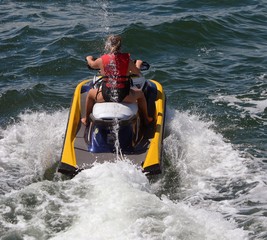 Young blond woman riding waves on a yellow jet ski.