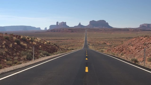 Cars driving along an empty straight road leading towards iconic butte and mesa mountains in Monument Valley, Utah USA. Travelers traveling into stunning desert Monument valley landmark landscape