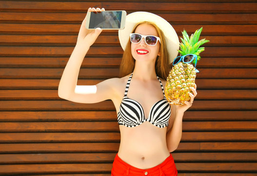 Pretty smiling woman with funny pineapple taking picture selfie on the smartphone