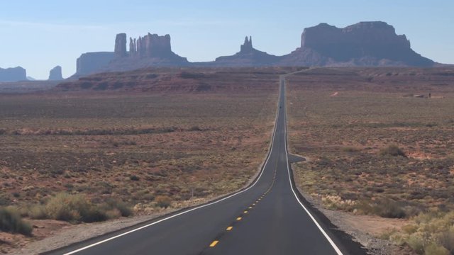 FIRST PERSON VIEW Driving along a straight empty road towards iconic Monument Valley landmark Utah USA. POV traveling on brand new highway road with yellow markings to Monument Valley desert landscape