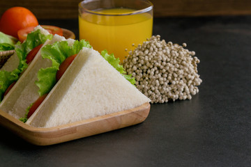 Piece of sandwich ham cheese with lettuce and tomato on wood plate. Homemade sandwich served with orange juice for breakfast or lunch. Delicious ham cheese sandwich ready to served on granite table.