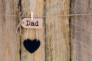 Father's Day - Dad on homemade paper label hanging with heart shape blackboard against rustic timber background