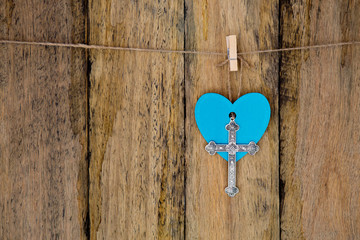 Silver metal crucifix hanging with a blue heart on string against rustic wooden background