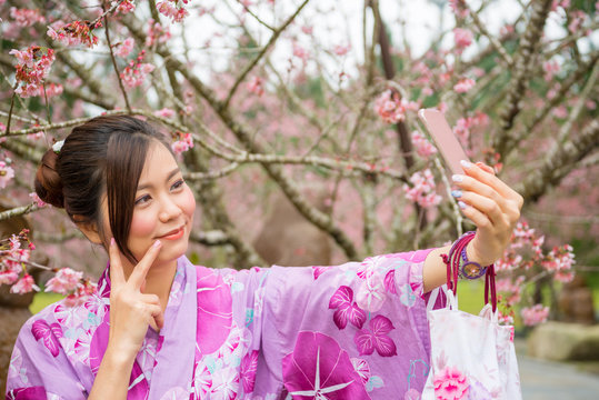 Asian girl taking selfie photo at sakura park