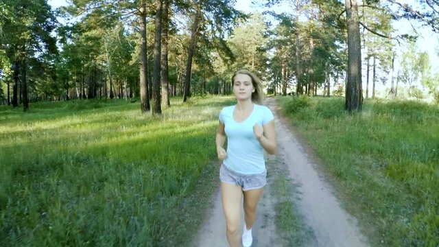 Young blonde girl jogging on country road. Running workout wellness concept. Slow motion. Sunshine.