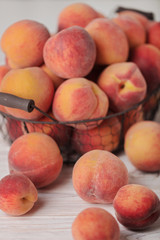 Ripe tasty peaches in a basket on a light wooden background.