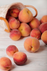 Ripe tasty peaches in a basket on a light wooden background.