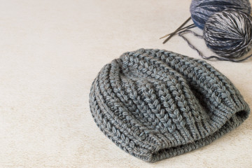 Hobby of manual knitting. A warm gray hat, balls wool fluffy yarn and knitting needles on a light background.