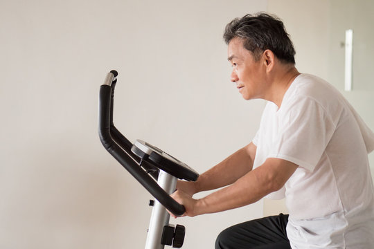 old senior man cycling, exercising, working out in gym with modern cycling machine