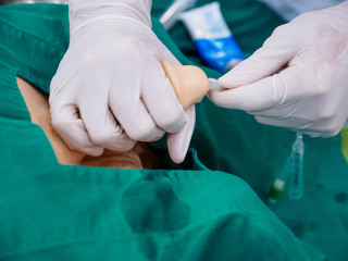 Close-up detail of a medical student inserting a foley catheter into the urethra of a dummy model's penis. Healthcare and education concept.