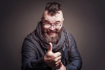 Smiling bearded man with a mohawk hairstyle showing thumb up on a brown background. Toned
