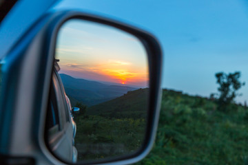 Sunset is reflected in the car's rear-view mirror