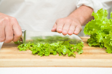 Chef's hands with knife cutting a green salad leaves on the wooden board. Preparation for cooking. Healthy eating and lifestyle.