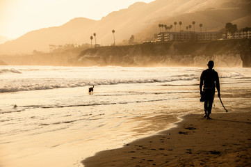 Fototapeta na wymiar Young man and man's best friend enjoying the beach sunset on a summer day