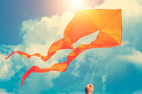 Orange kite in hand in sunny blue sky with clouds