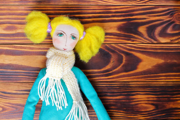 Soft handmade doll from textile of cute girl with bright yellow hair in coat and a scarf on wooden boards