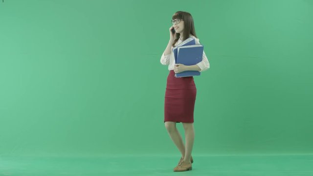 Attractive business woman walks with folders in hands and answers a phone call