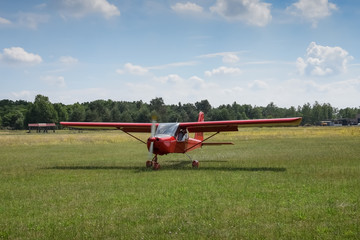 Fototapeta na wymiar Light aircraft. Light red school airplane on airport grass after landing. The propeller rotates