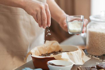 Woman sprinkling desiccated coconut into baking dish with delicious rice dessert on table