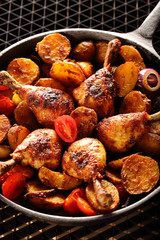 Roasted chicken legs with baked potato on frying pan