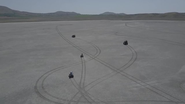 Aerial view of ATV driving down a beautiful wide open beach with crashing ocean waves slow motion
