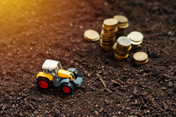 Agricultural tractor toy and golden coins on fertile soil land