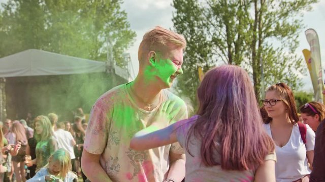 Young people smearing each other with powder paint during the color Holi Festival. Medium shot