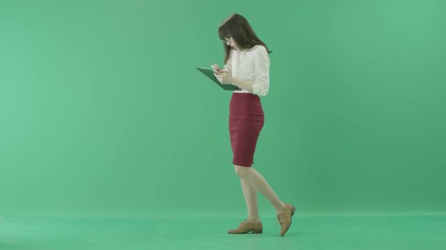 Young business woman walks with a clipboard speaking on a cellphone and making notes