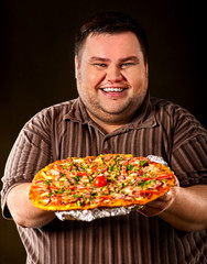 Fat man eating fast food and offers great pizza to customers and friends. Breakfast for overweight person. leads to obesity. Person regularly overeats concept on dark background.
