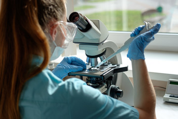 woman laborant working with microscope holding automatic pipette