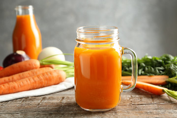 Composition with mason jar of fresh carrot juice with vegetables on wooden table
