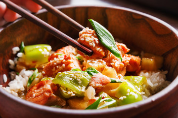 Asian cuisine - rice in sauce with stir fried vegetables, pineapple and salmon. Wooden bowl with chopsticks. Close up.